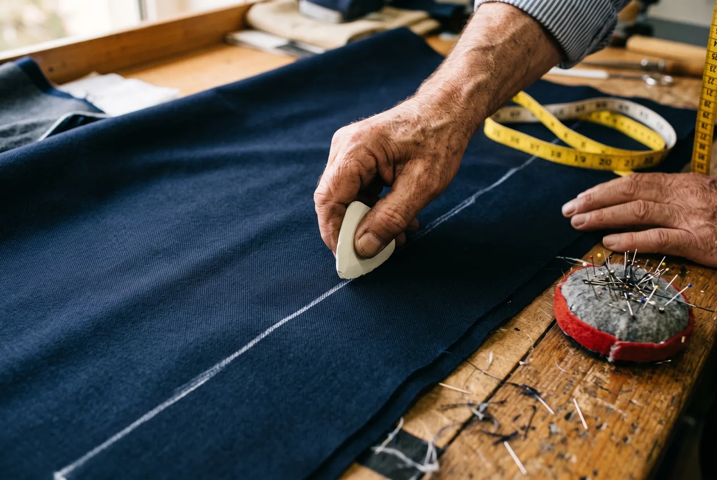 A tailor marking navy fabric beside a measuring tape and pin cushion